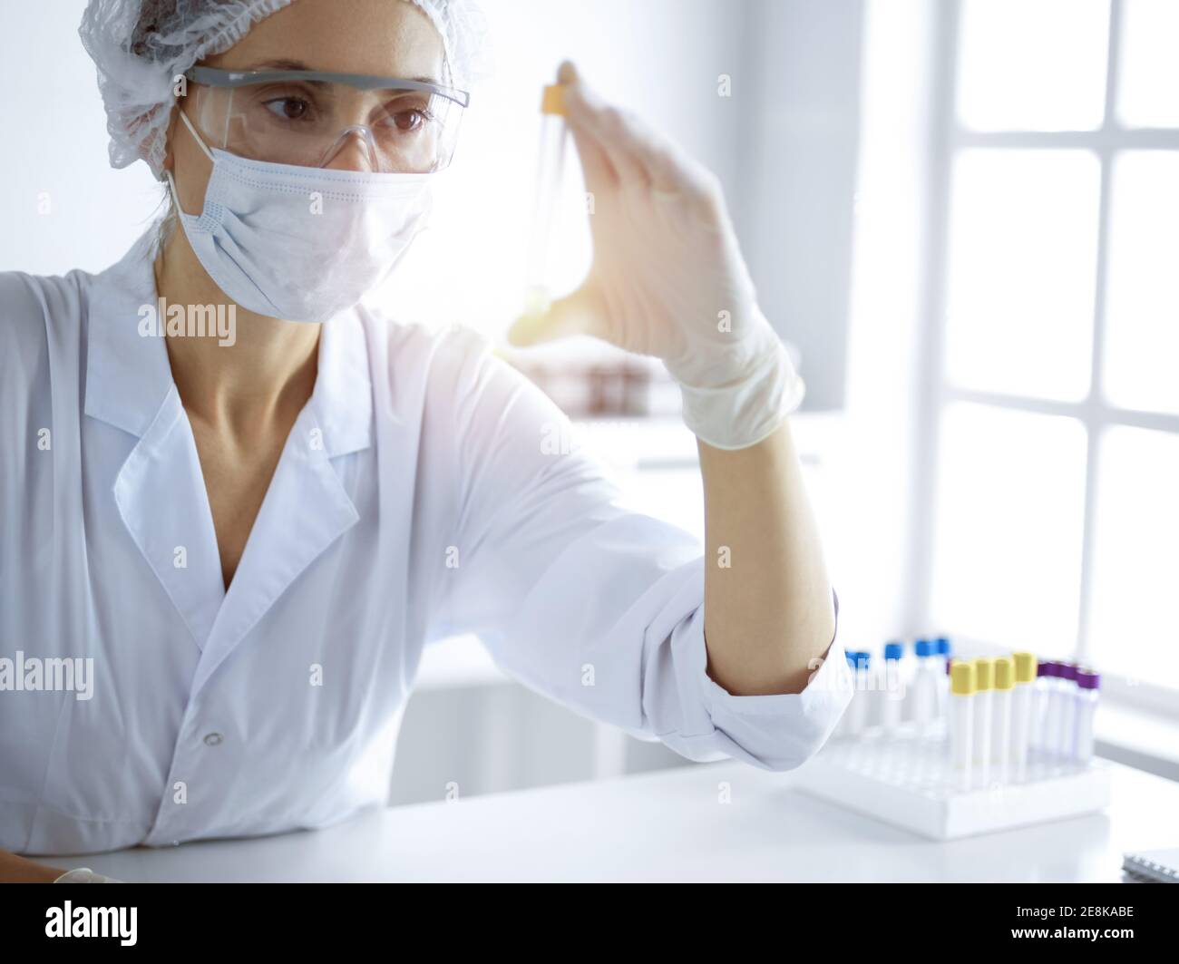 Professional female scientist in protective eyeglasses researching tube