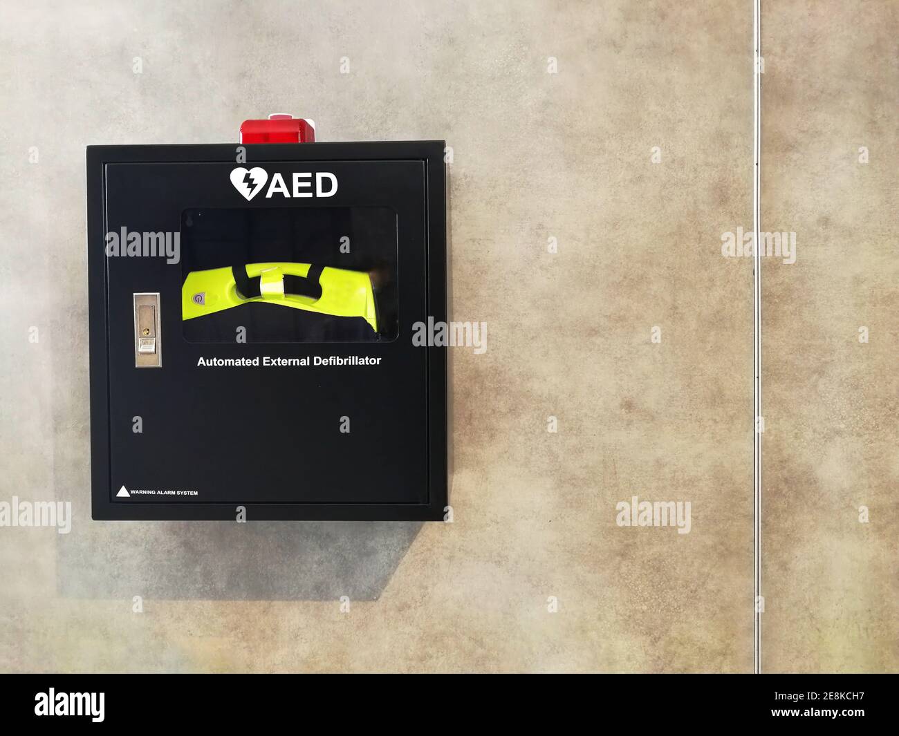 Automated External Defibrillator, AED black box with Red LED Alarm on on bare cement or concrete wall Stock Photo