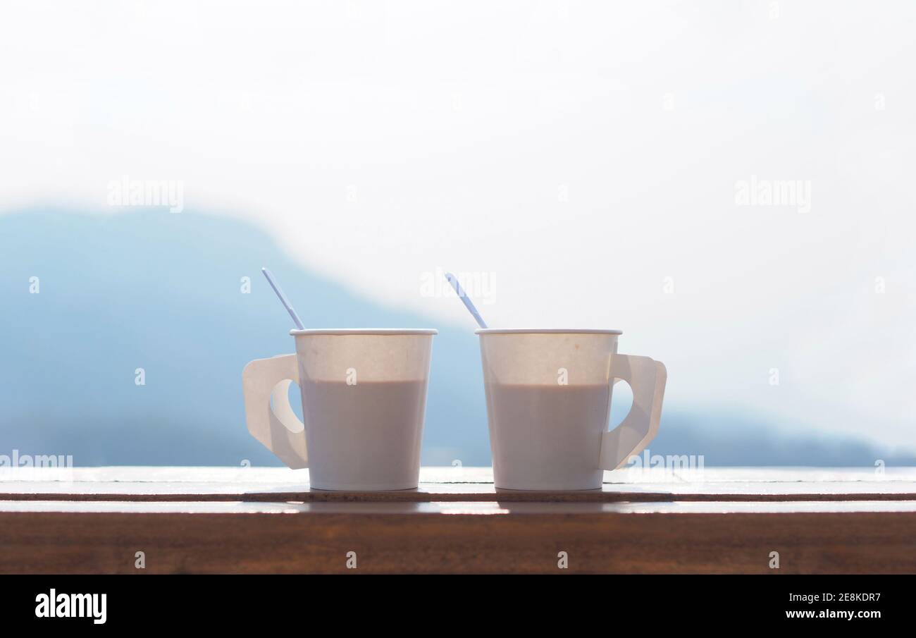Coffee in a paper cup on a wooden table in the morning with Blurred Mountain background and copy space on top of image. Stock Photo