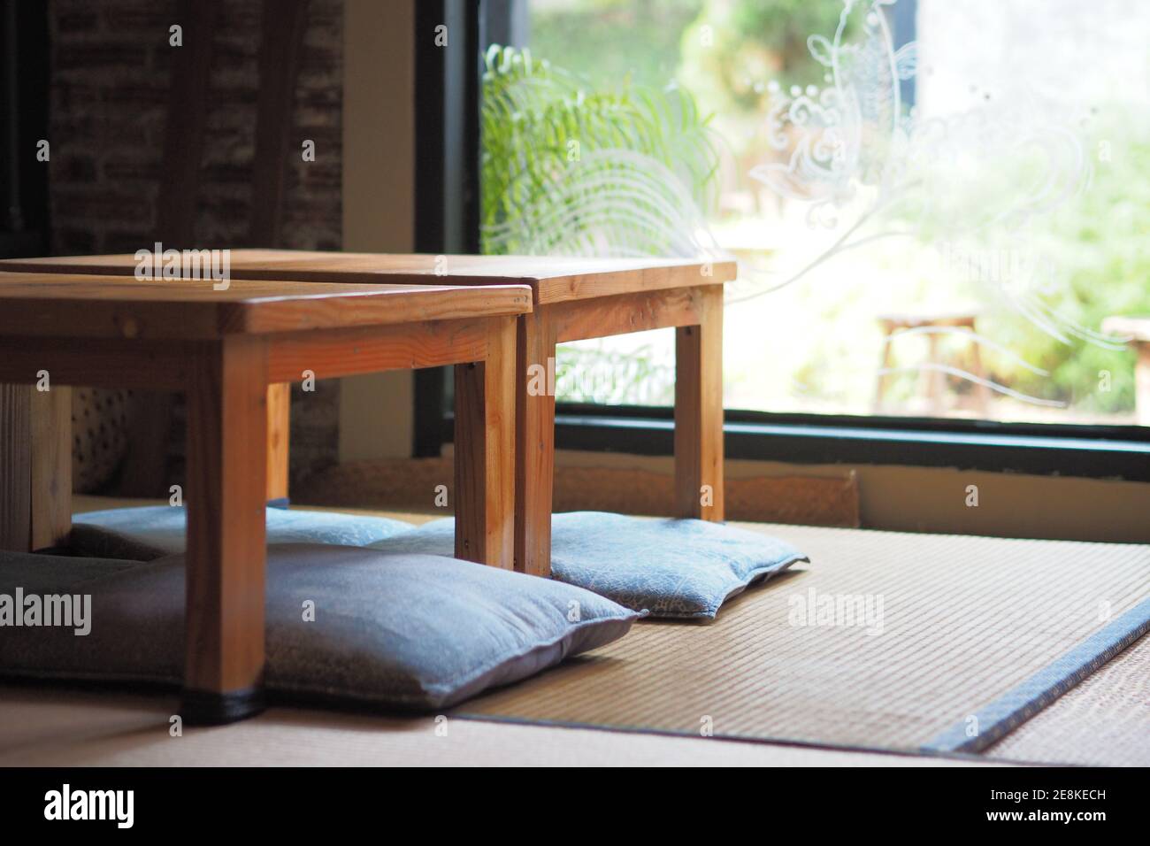 Japanese-style room decoration with wooden tables and sitting cushions floor, Green garden background. Stock Photo