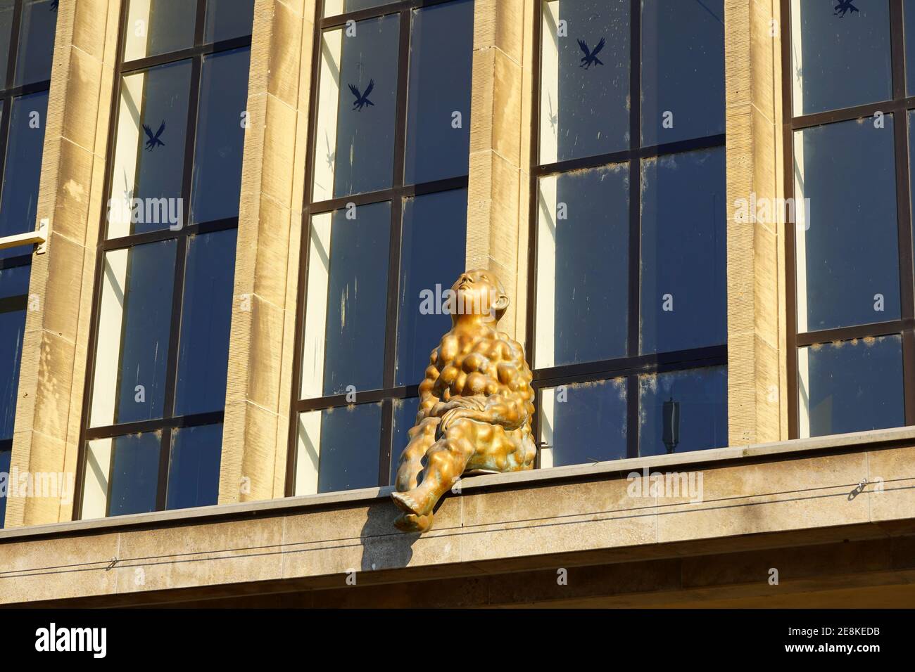 The bronze sculpture 'Beulenmann' (bump man), sitting in front of a window of the Main Station building in Düsseldorf. Artwork by Paloma Varga Weisz. Stock Photo