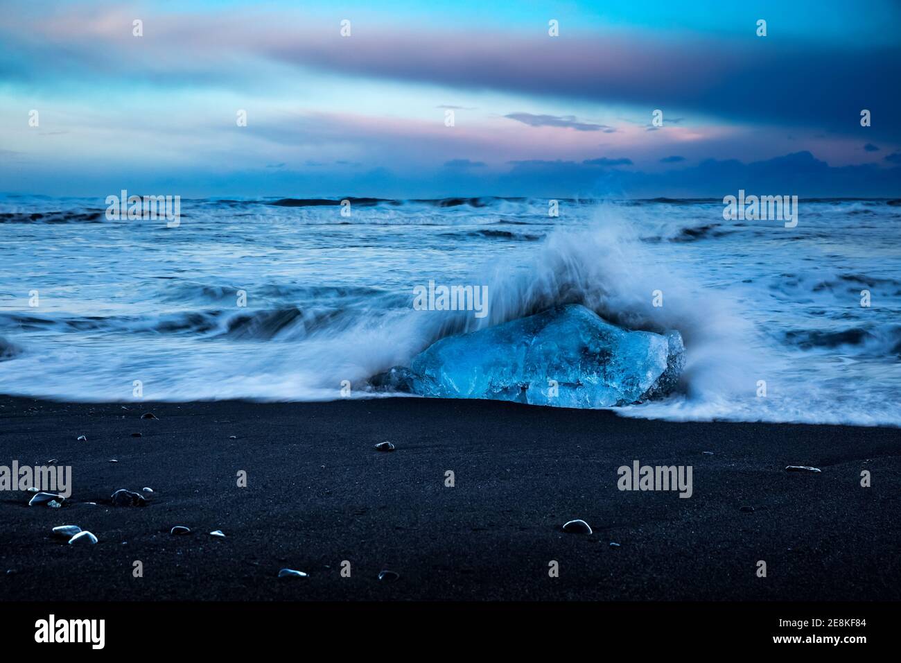 Beautiful Landscape of a Black Volcanic Sand Beach with Icebergs. Waves Against a Large Block of Ice on the Shore. Amazing Nature of Vatnajokull Stock Photo
