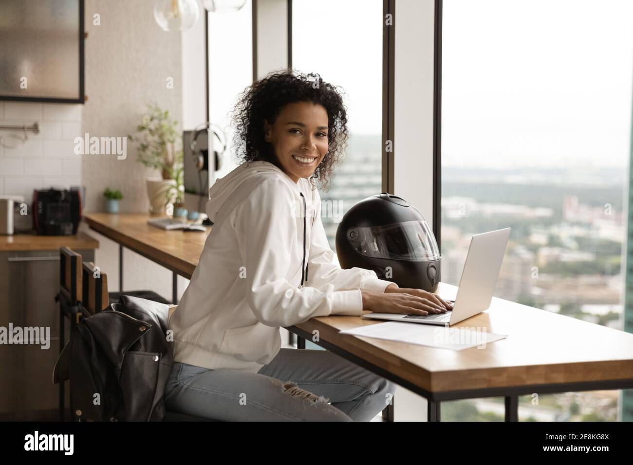 Smiling black woman biker sit by laptop in stylish apartment Stock Photo