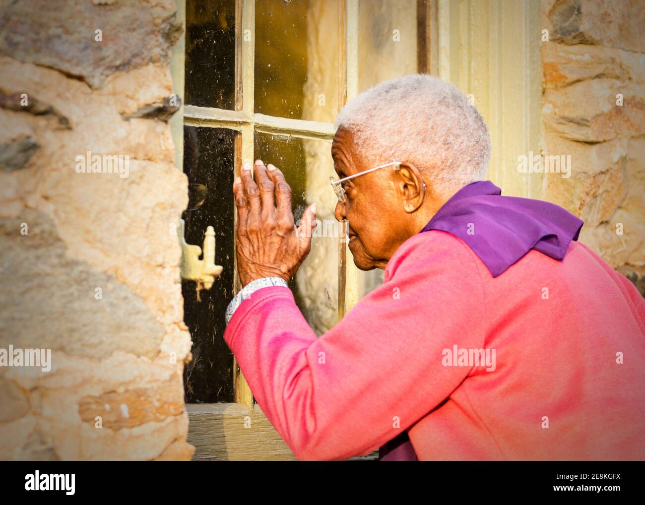 90-year-old elderly woman looking through the window of a historic church that she attended many years ago in Waterford Virginia. Stock Photo