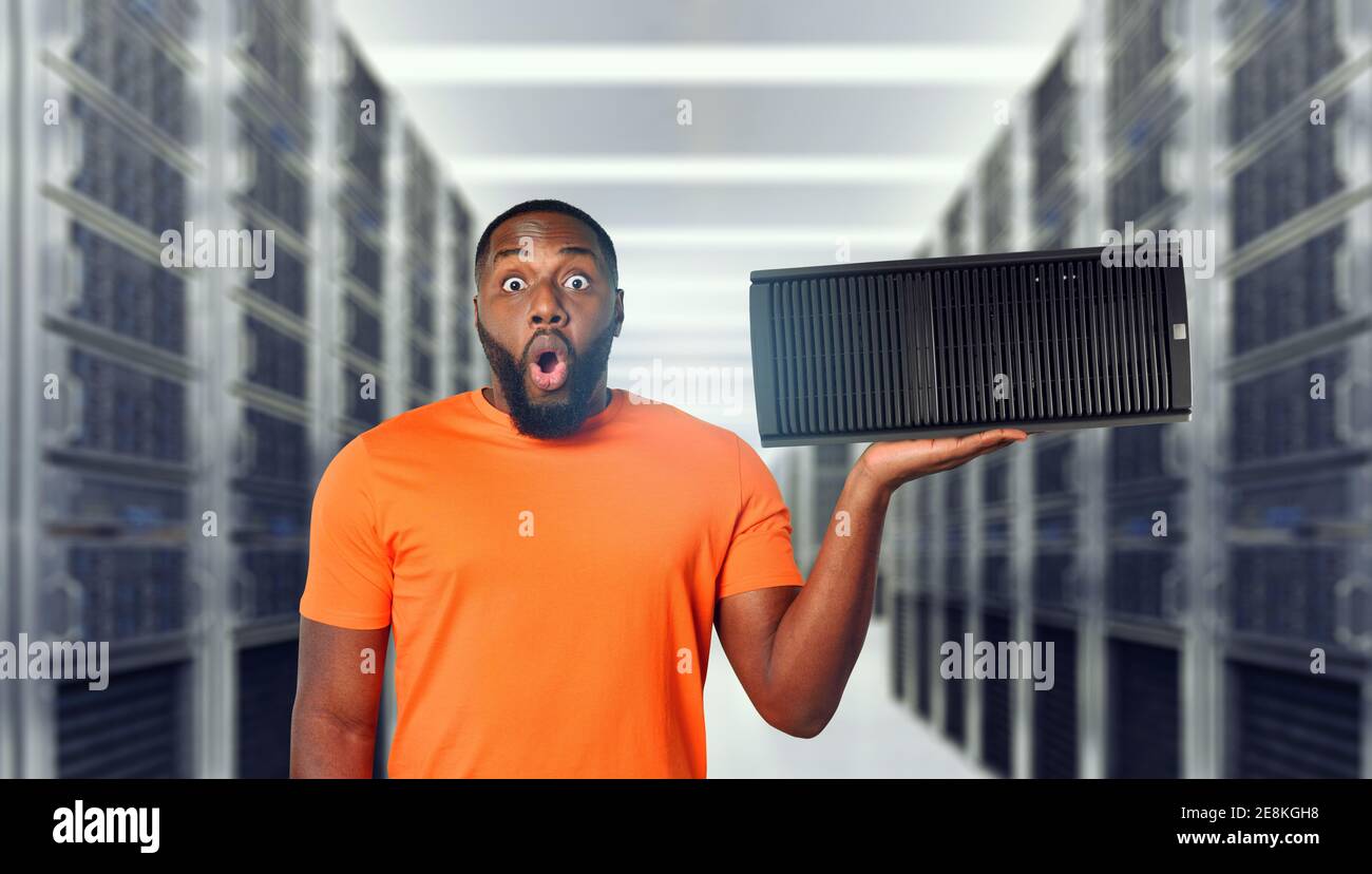 Surprised black man holds a server in hand. Concept of hosting and storage Stock Photo