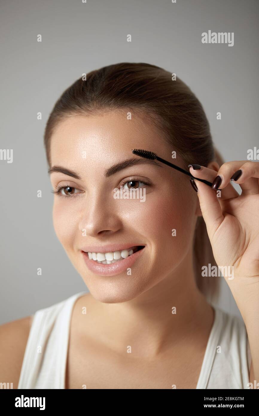 Beauty makeup. Beautiful  Woman shaping eyebrow closeup. Girl model with professional makeup using eyebrows brush and smiling Stock Photo