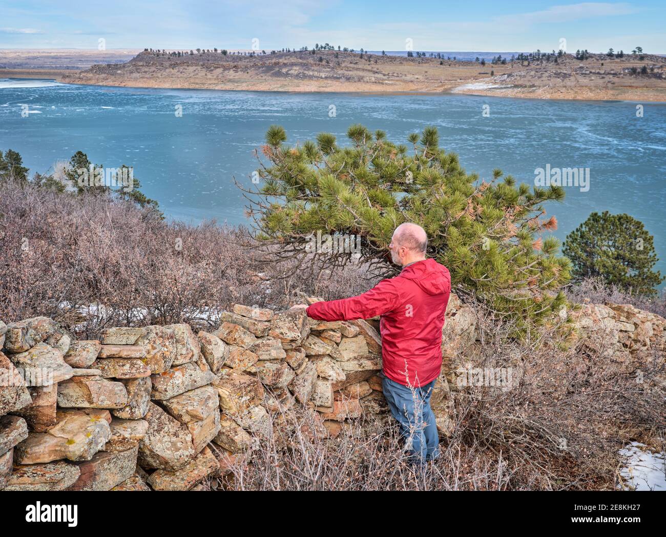 senior hiker at old stone fence overlooking frozen mountain lake  - Horsetooth Reservoir at foothills of Rocky Mountains - a popular recreational area Stock Photo