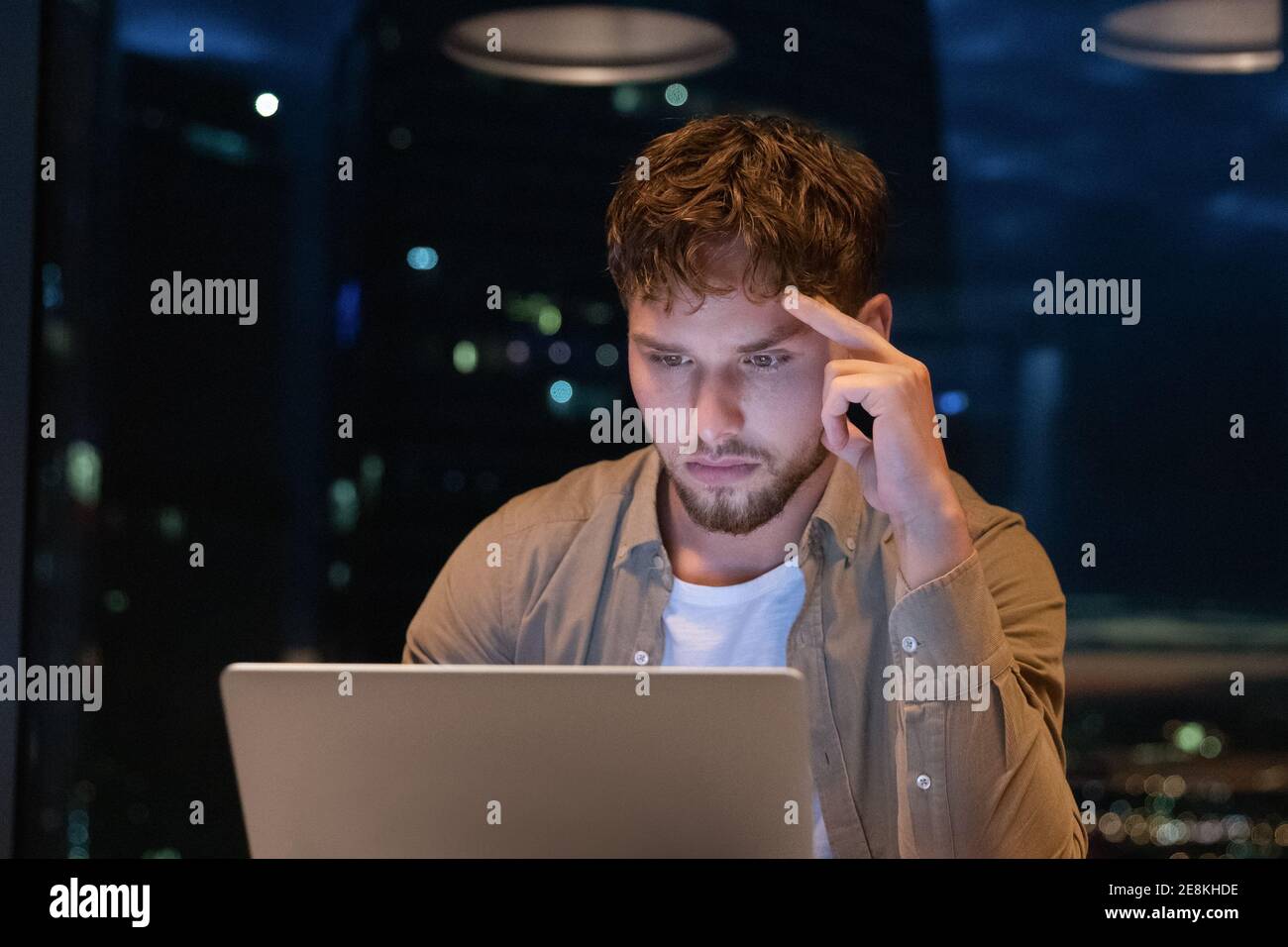 Young man analyst working until late hours by pc screen Stock Photo
