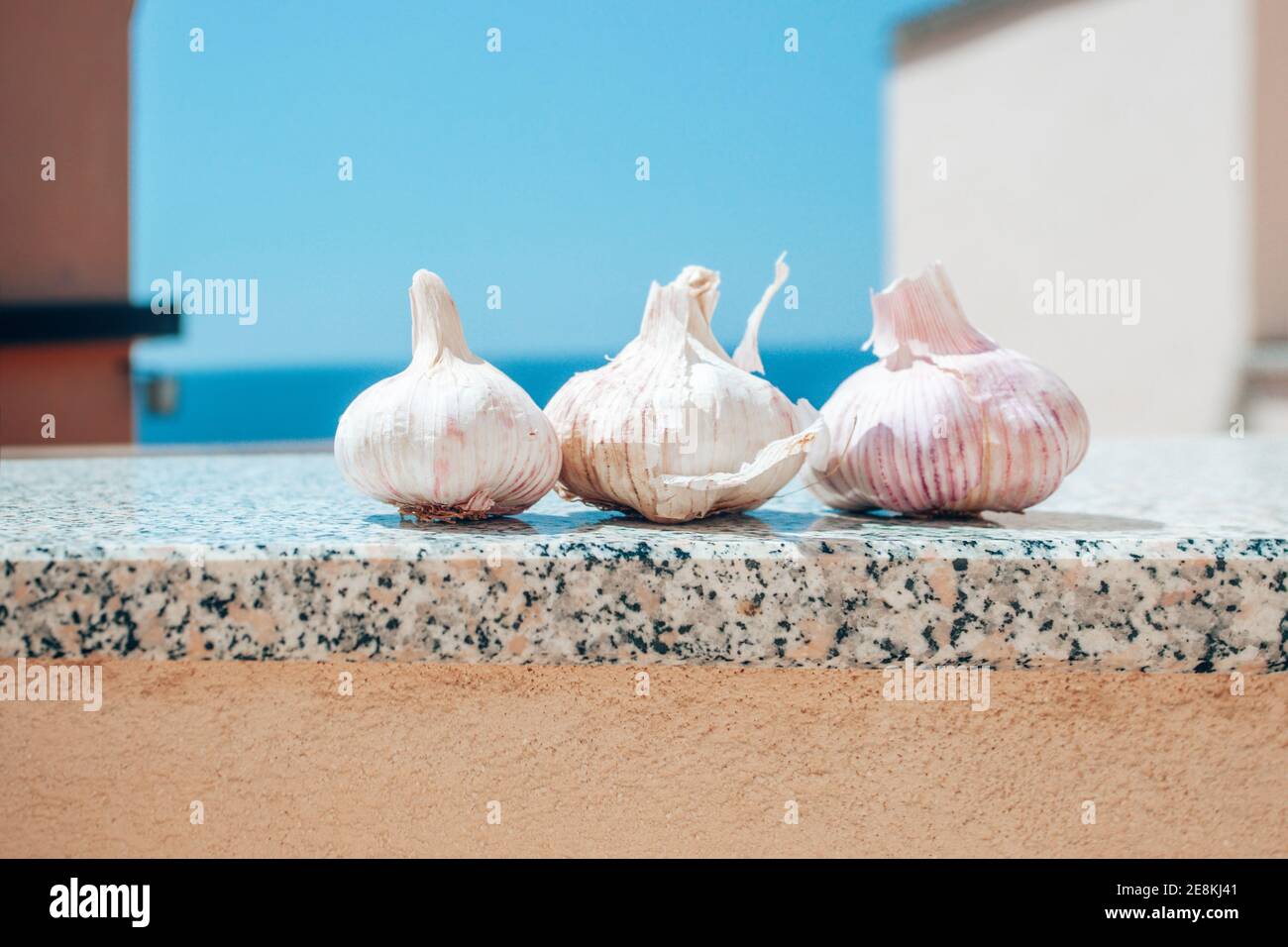 Conceptual realism: three garlic raw heads on architectural marble podium against sea under the sun Stock Photo