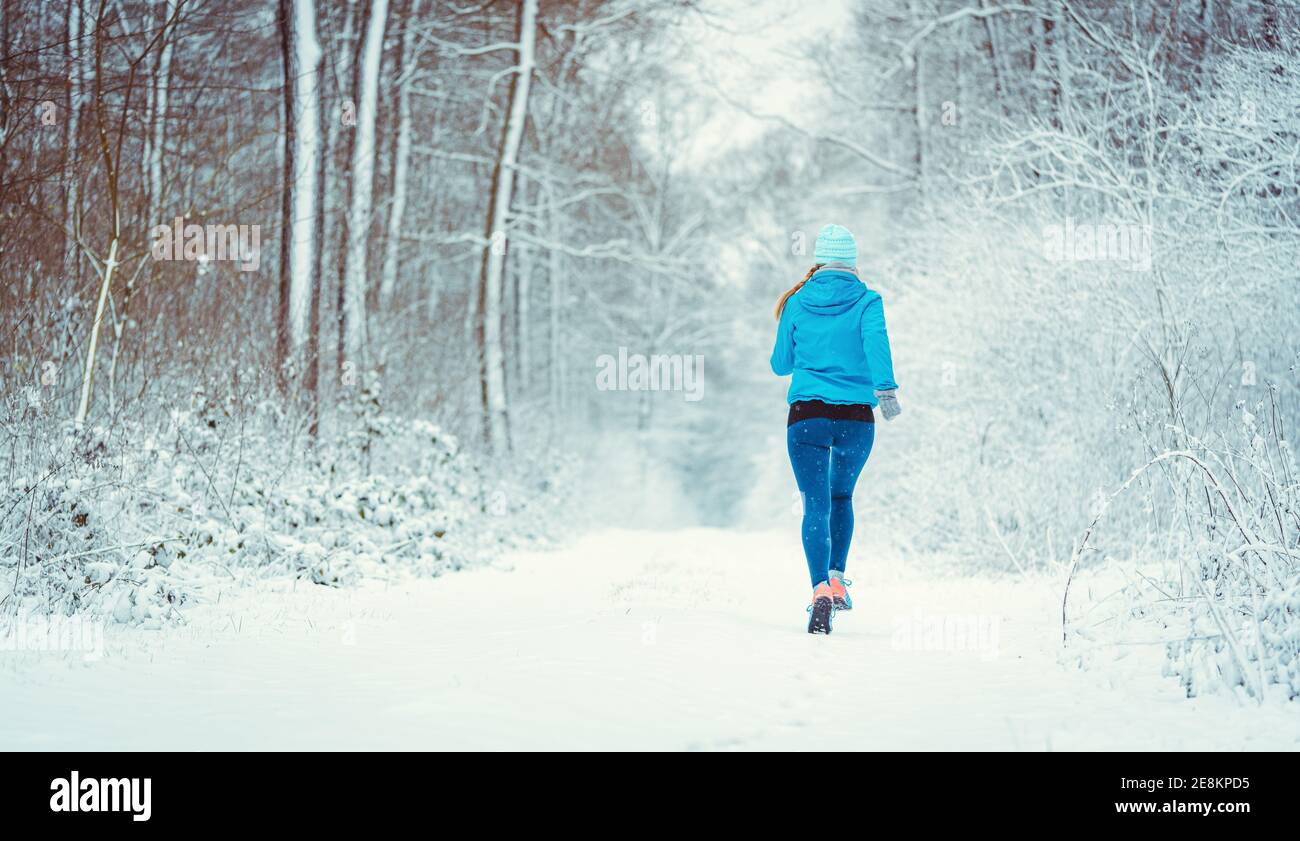 Young woman running down a path in the winter woods through snow Stock Photo