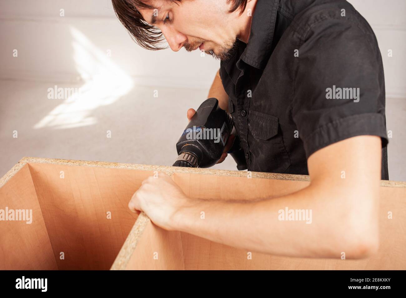 A man drills a hole in a closet using a drill. Stock Photo