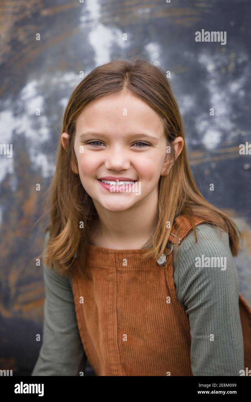 Young girl in a brown overall dress in the winter sitting near an urban