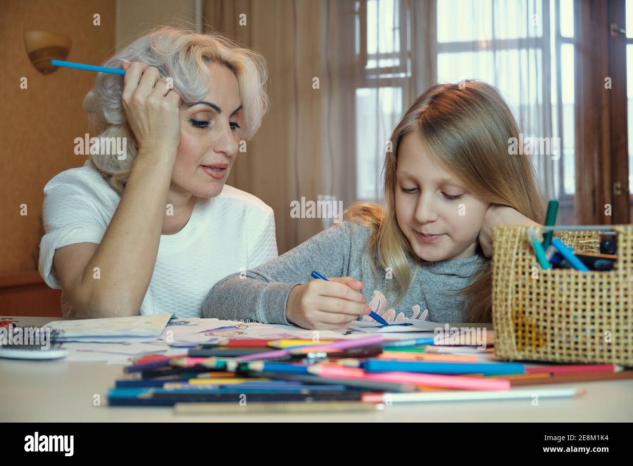 Mature mother and her little daughter drawing together, doing homework at home, selective focus Stock Photo