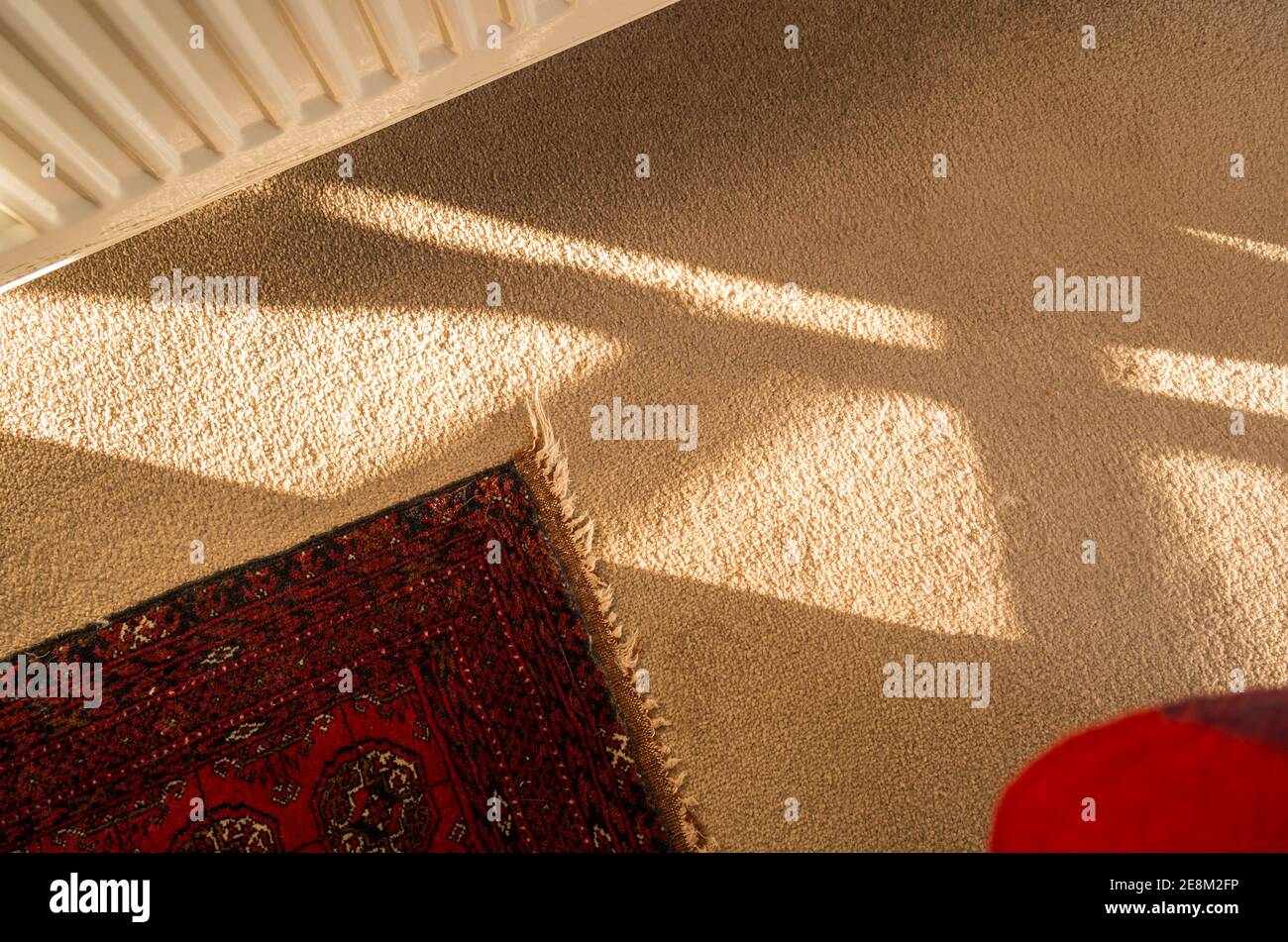Shapes and shadows with fragments of a central heating radiator, woollen carpet, Persian rug  and a splash of red in an English home Stock Photo