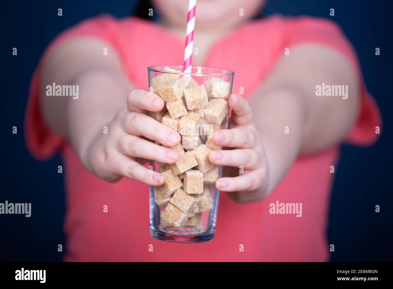 Child holding a glass full of sugar cubes. Everyday sugar usage among children concept Stock Photo