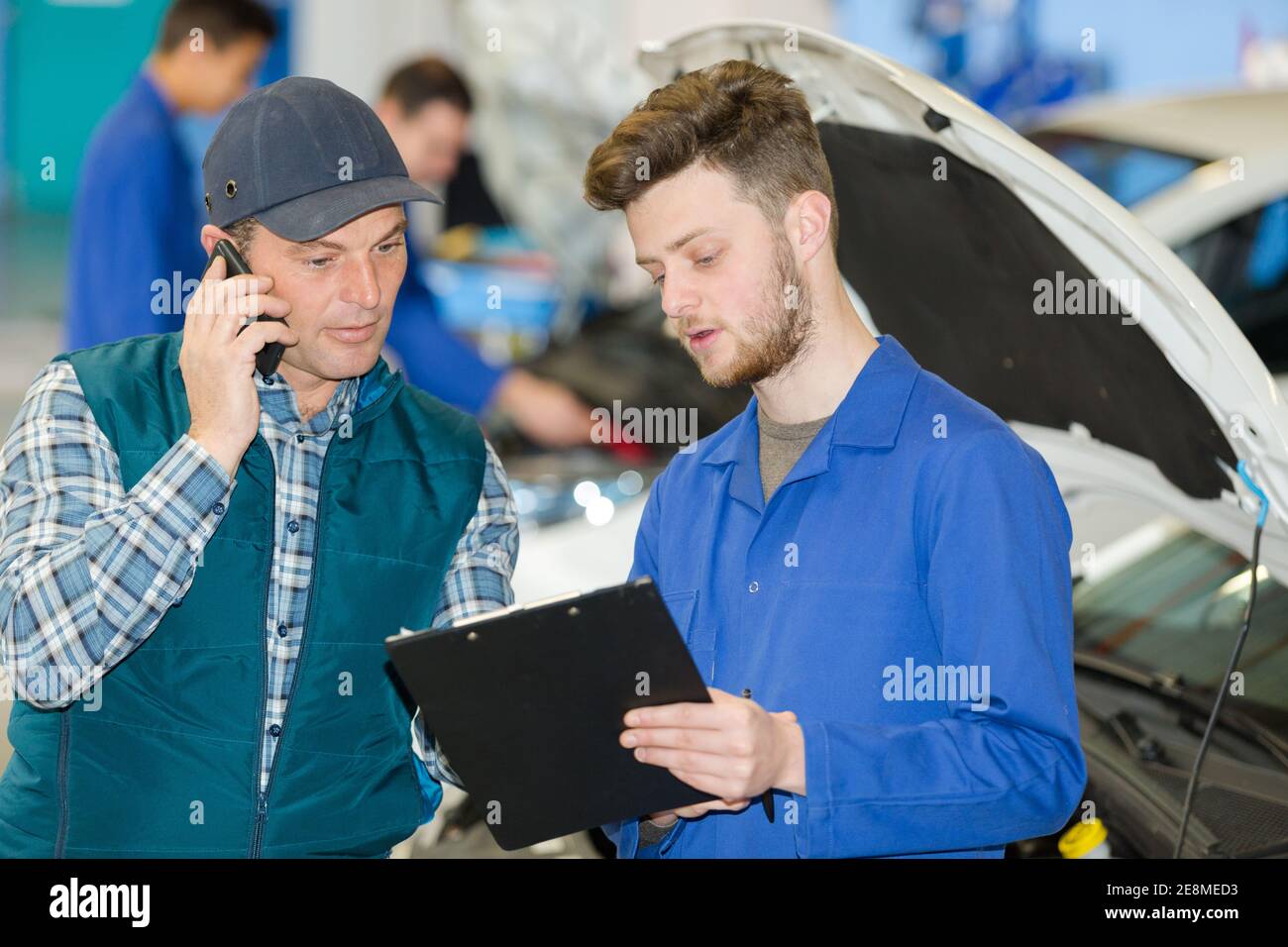 apprentice mechanic talking to man using smartphone Stock Photo