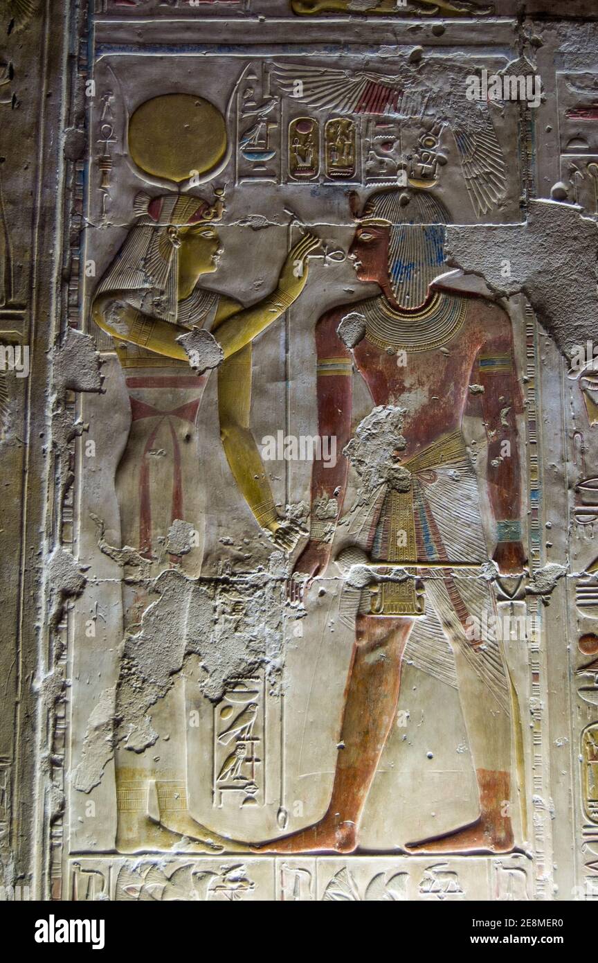 Ancient Egyptian bas relief carving showing the goddess Hathor, wearing a crown of horns, putting the sacred ankh to the face of Pharaoh Seti I. Abydo Stock Photo