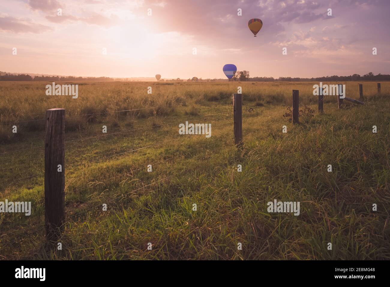 Golden sunlight on a summer morning cast over a scenic rural landscape as tourist hot air balloons approach for landing in the Hunter Valley region, r Stock Photo