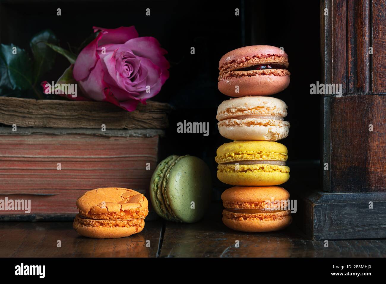 Stack of delicious classic french macaroons, an old book and a rose on vintage dark sideboard Stock Photo