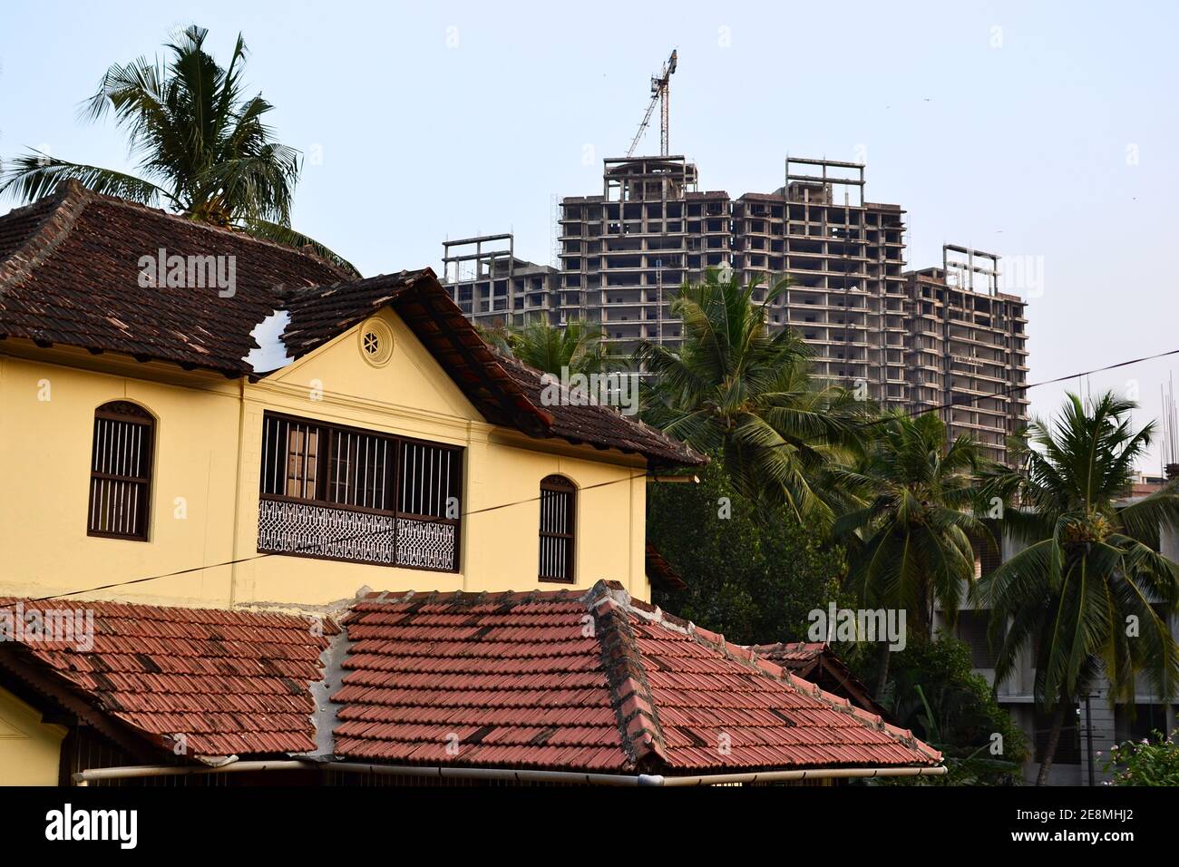 Old colonial building with shingle roof and construction site with crane on the background, Mangalore, India Stock Photo
