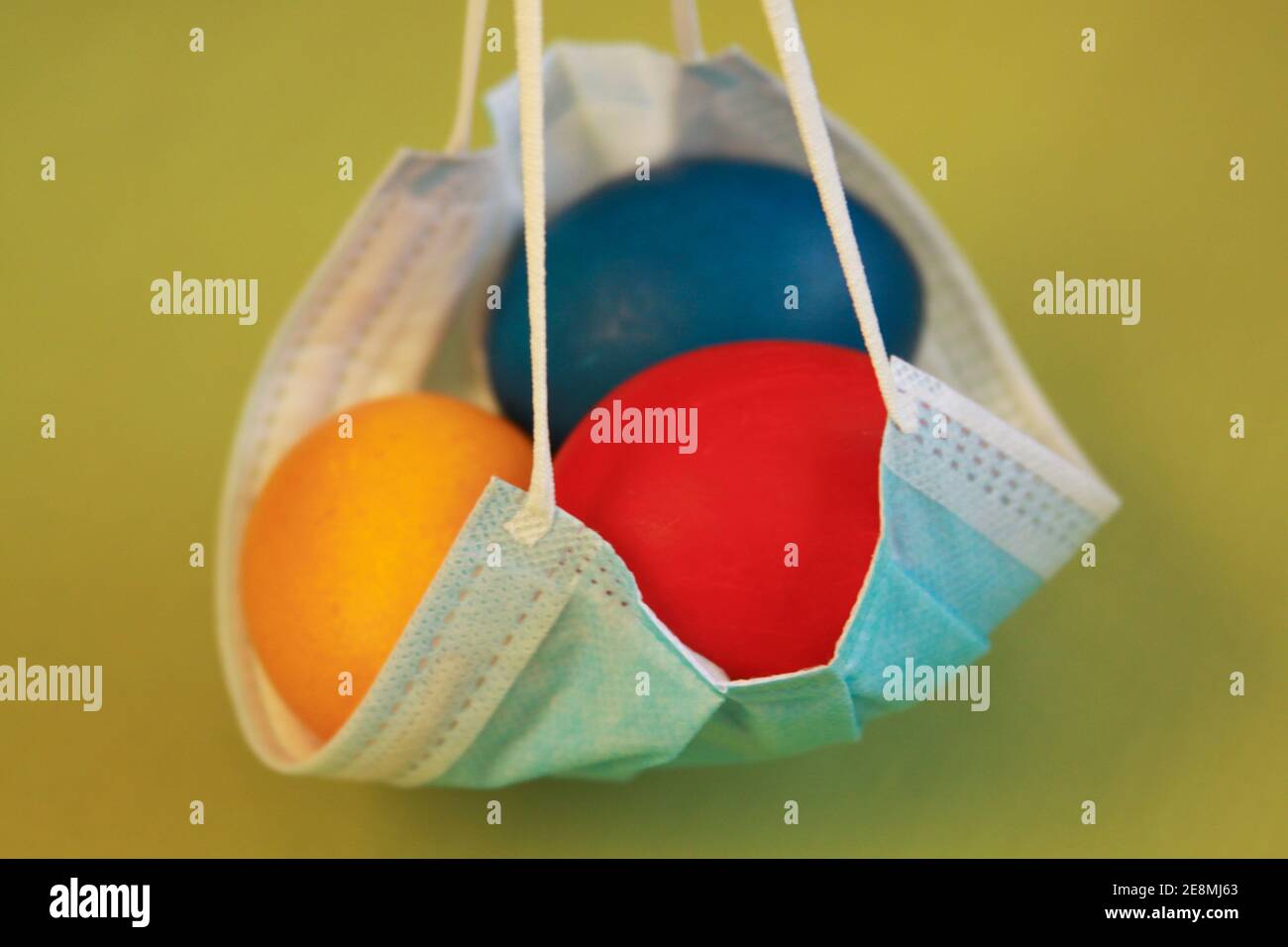 Isolated colored painted Easter eggs in surgical mask, a symbol of coronavirus pandemic. Safety first while celebrating Easter 2020 covid 19 outbreak Stock Photo