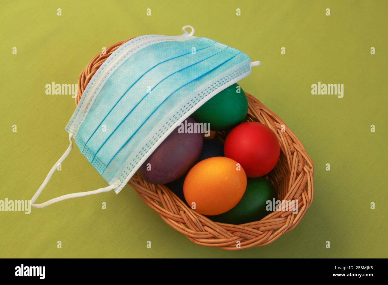 Isolated colored painted Easter eggs in wooden basket decoration with surgical mask, a symbol of coronavirus pandemic. Easter 2020 covid 19 outbreak c Stock Photo