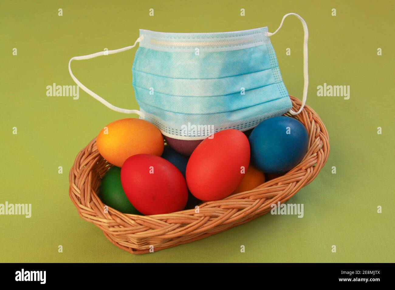 Isolated colored painted Easter eggs in wooden basket decoration with surgical mask, a symbol of coronavirus pandemic. Easter 2020 covid 19 outbreak c Stock Photo