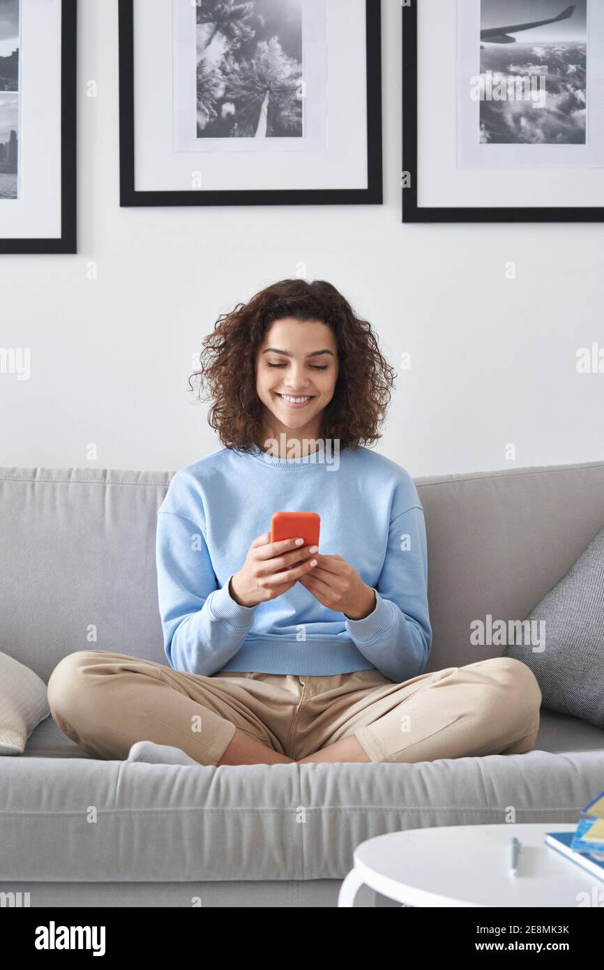Smiling latin teen girl holding smartphone using mobile apps at home. Stock Photo