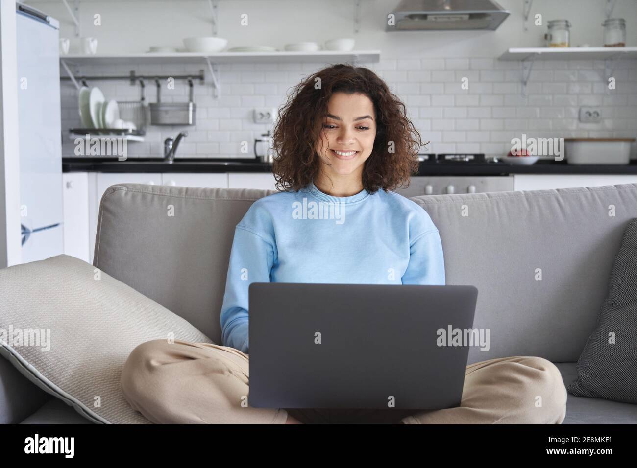 Happy hispanic teen girl using laptop computer sitting on sofa at home ...