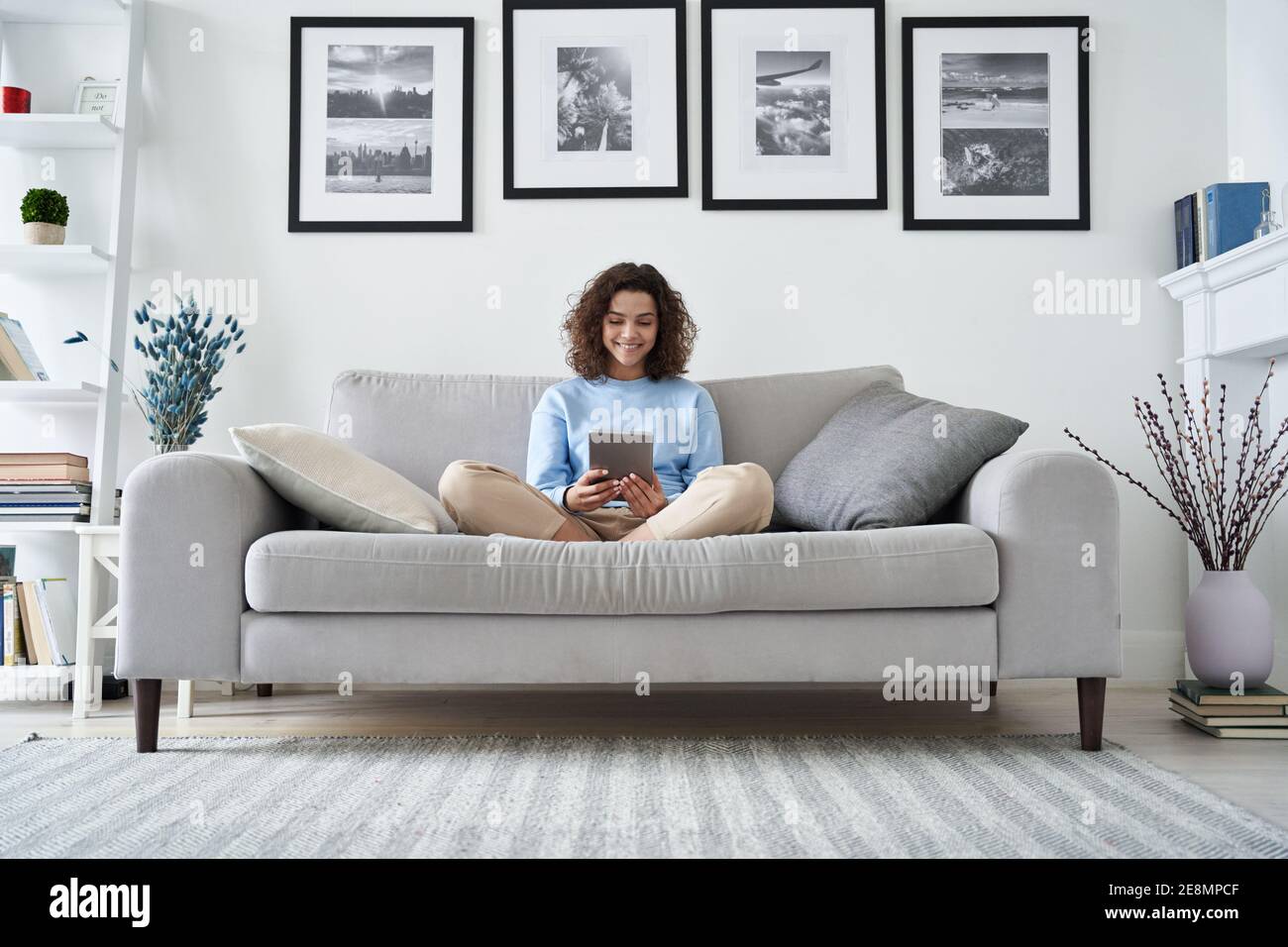 Happy hispanic teen girl using digital tablet sitting on couch at home. Stock Photo