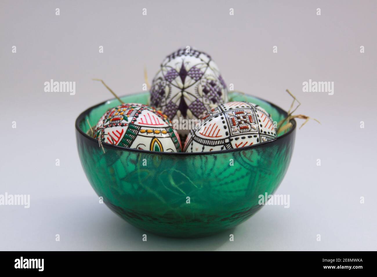 Isolated traditional handmade Easter eggs in glass bowl on hay. Hand wax painting technique from Bucovina, Romania used to decorate Easter eggs in Mol Stock Photo