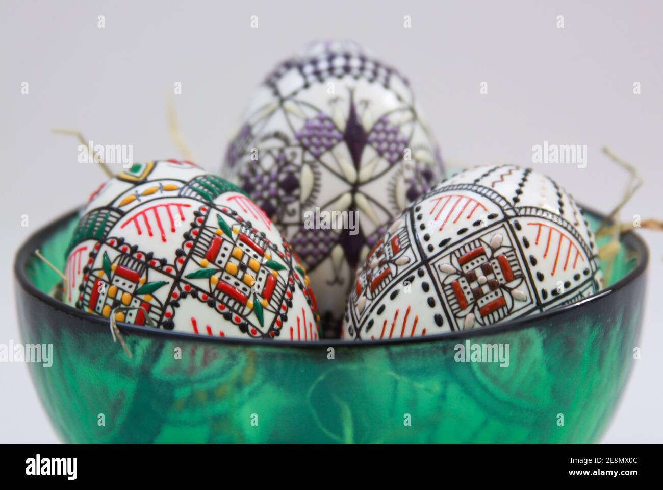 Isolated traditional handmade Easter eggs in glass bowl on hay. Hand wax painting technique from Bucovina, Romania used to decorate Easter eggs in Mol Stock Photo