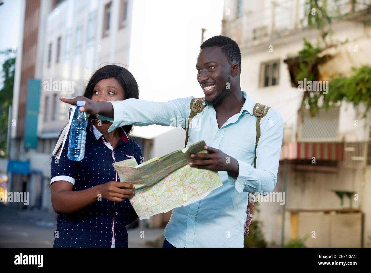 young tourist standing outdoors showing something to his friend with map in hand smiling Stock Photo