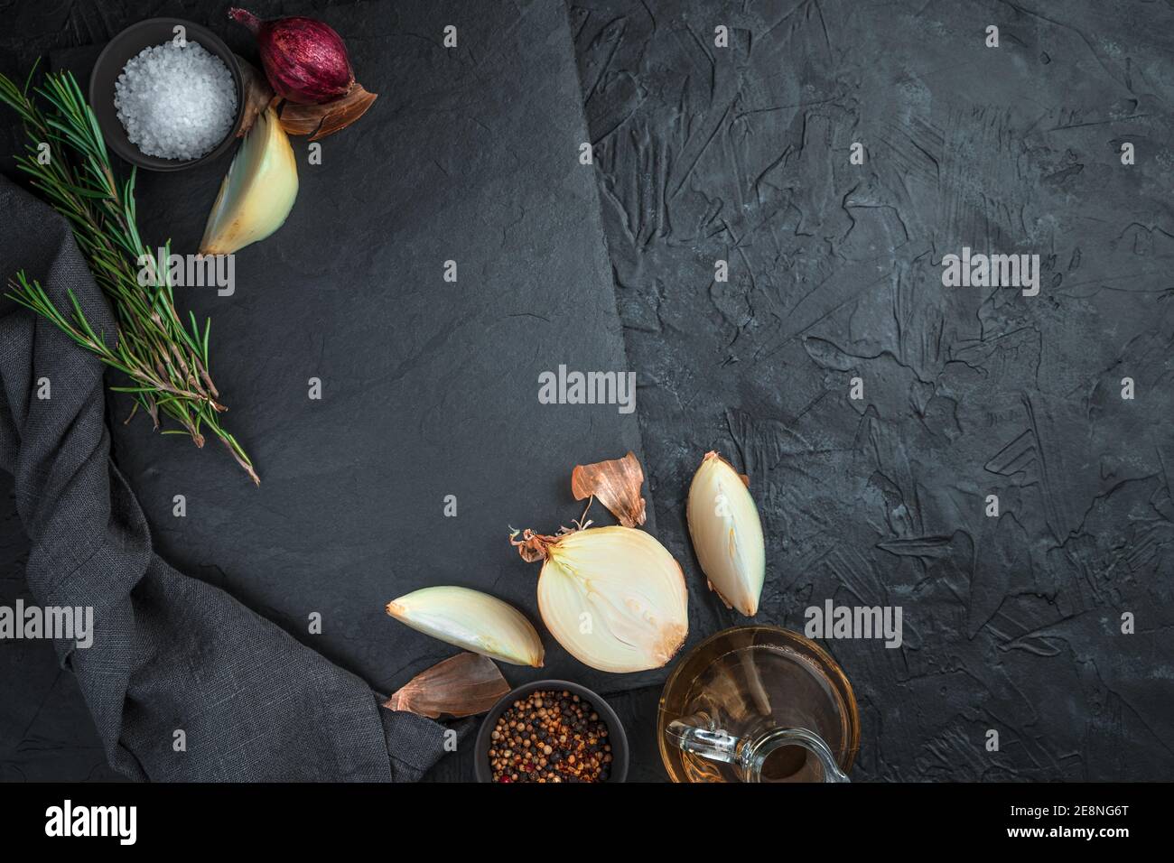 An empty, flat, rectangular dish, surrounded by onions, spices and rosemary on a black background. Stock Photo