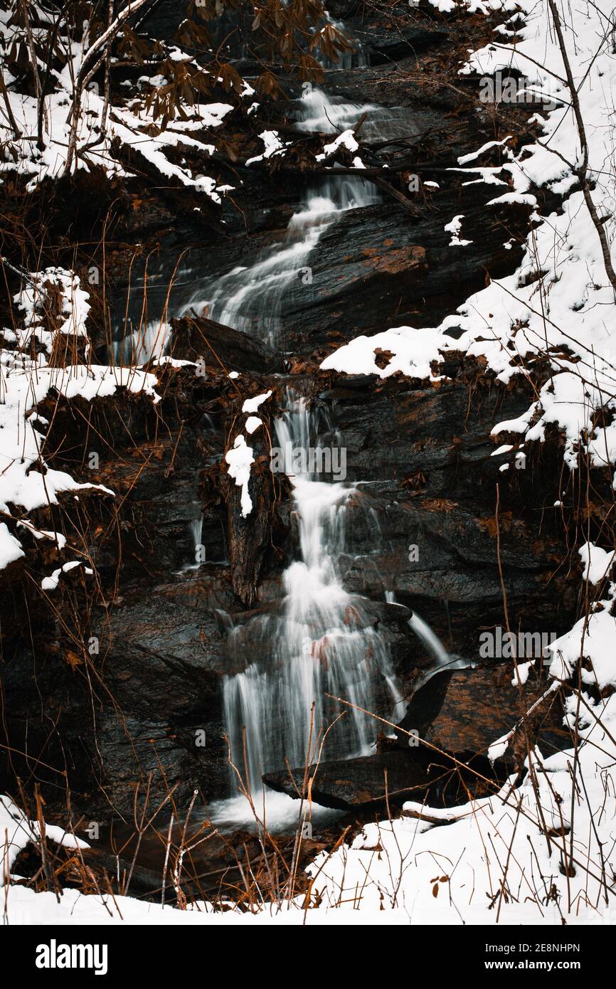 A vertical shot of a waterfall flowing through rocky cliffs covered in ...