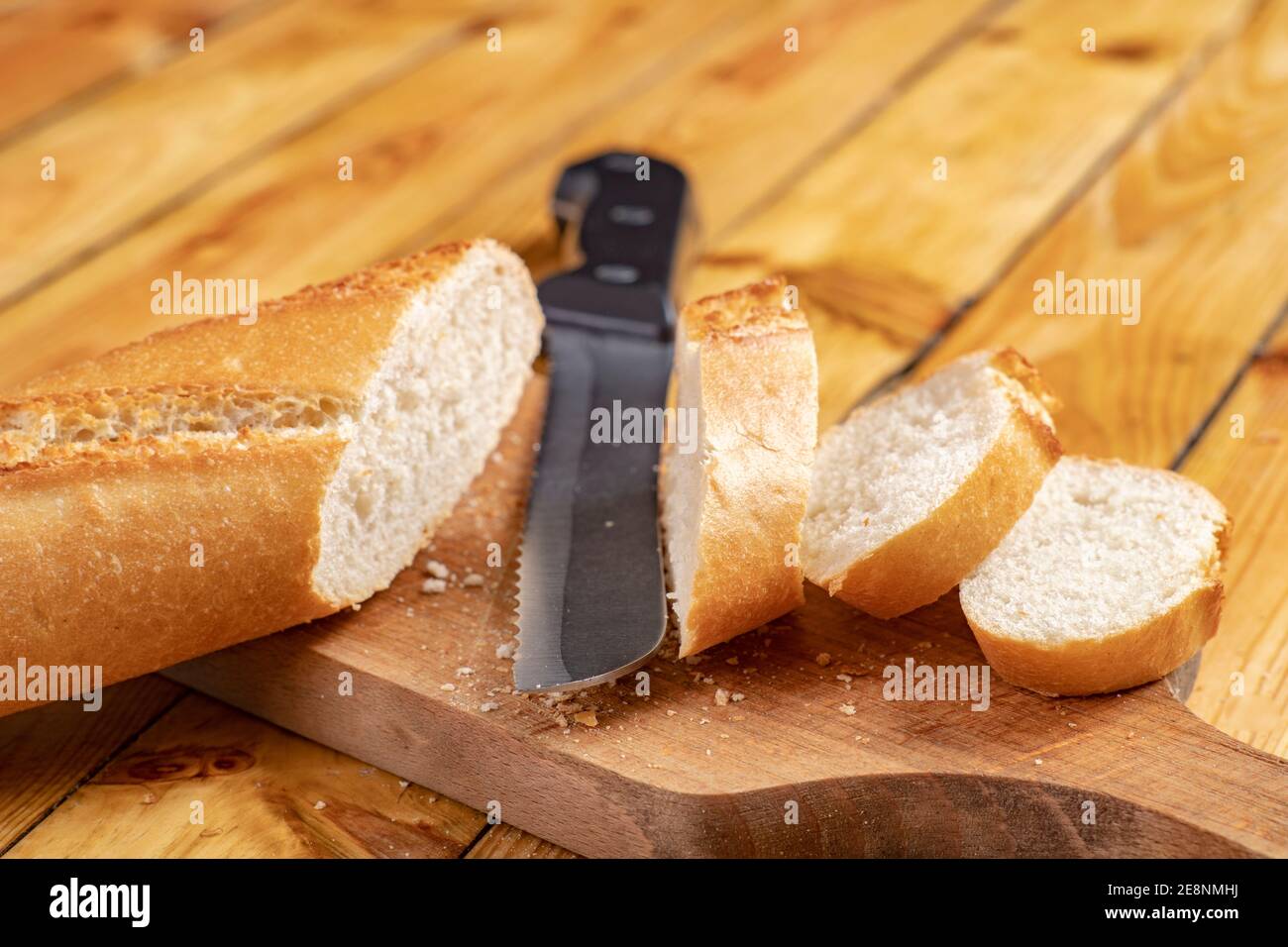 Tasty and fresh baguette cut into pieces. Bread and a chopping knife in the home kitchen. Light background. Stock Photo