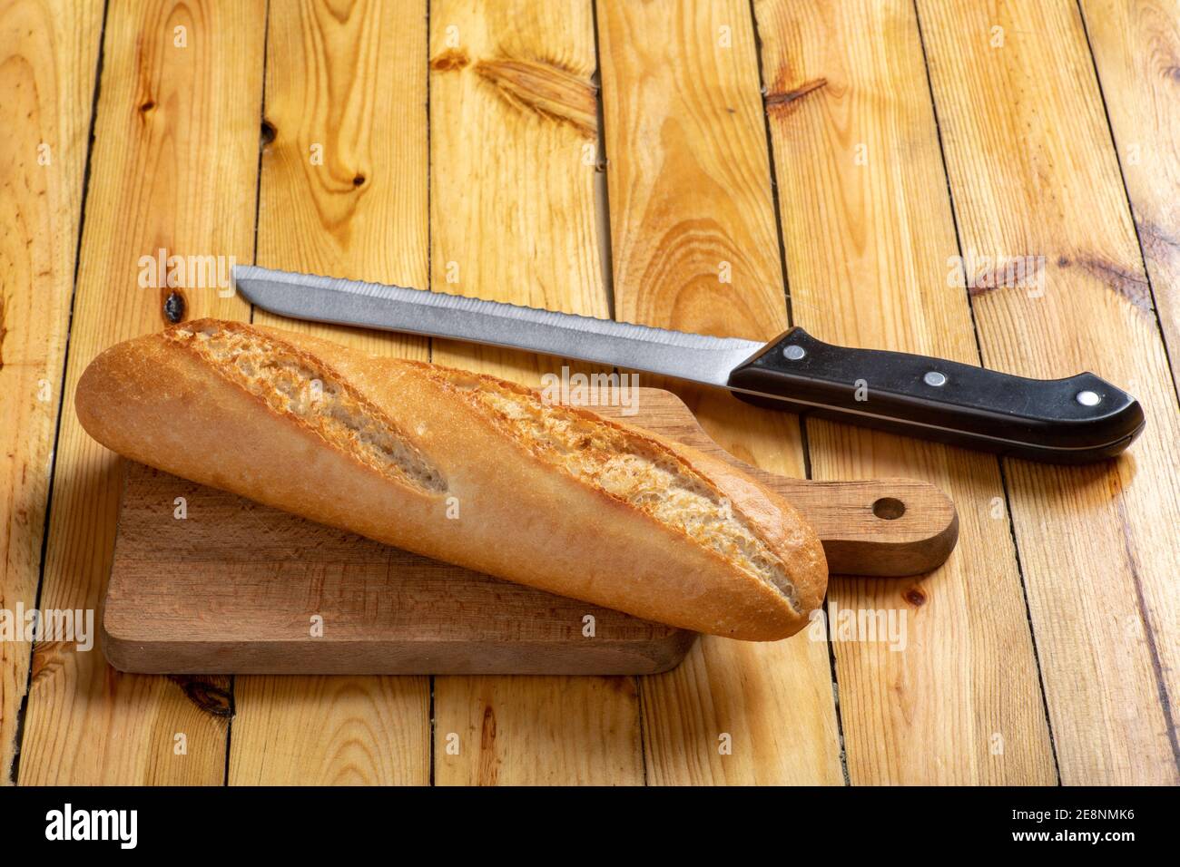 Tasty and fresh baguette on the kitchen table. Bread and a chopping knife in the home kitchen. Light background. Stock Photo