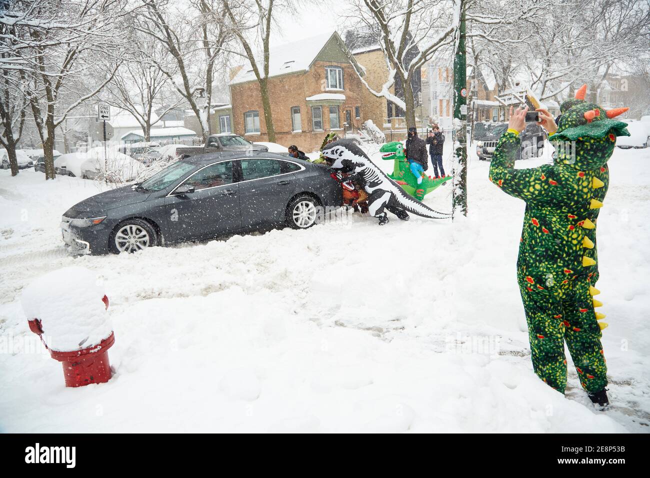 Neighbors attending a dinosaur-themed children's birthday party step in to help a stuck motorist in Chicago, Illinois during a winter snow storm. Stock Photo