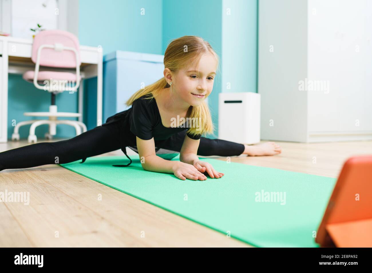 Primary school age sportive gymnast girl in black leotard stay in twine