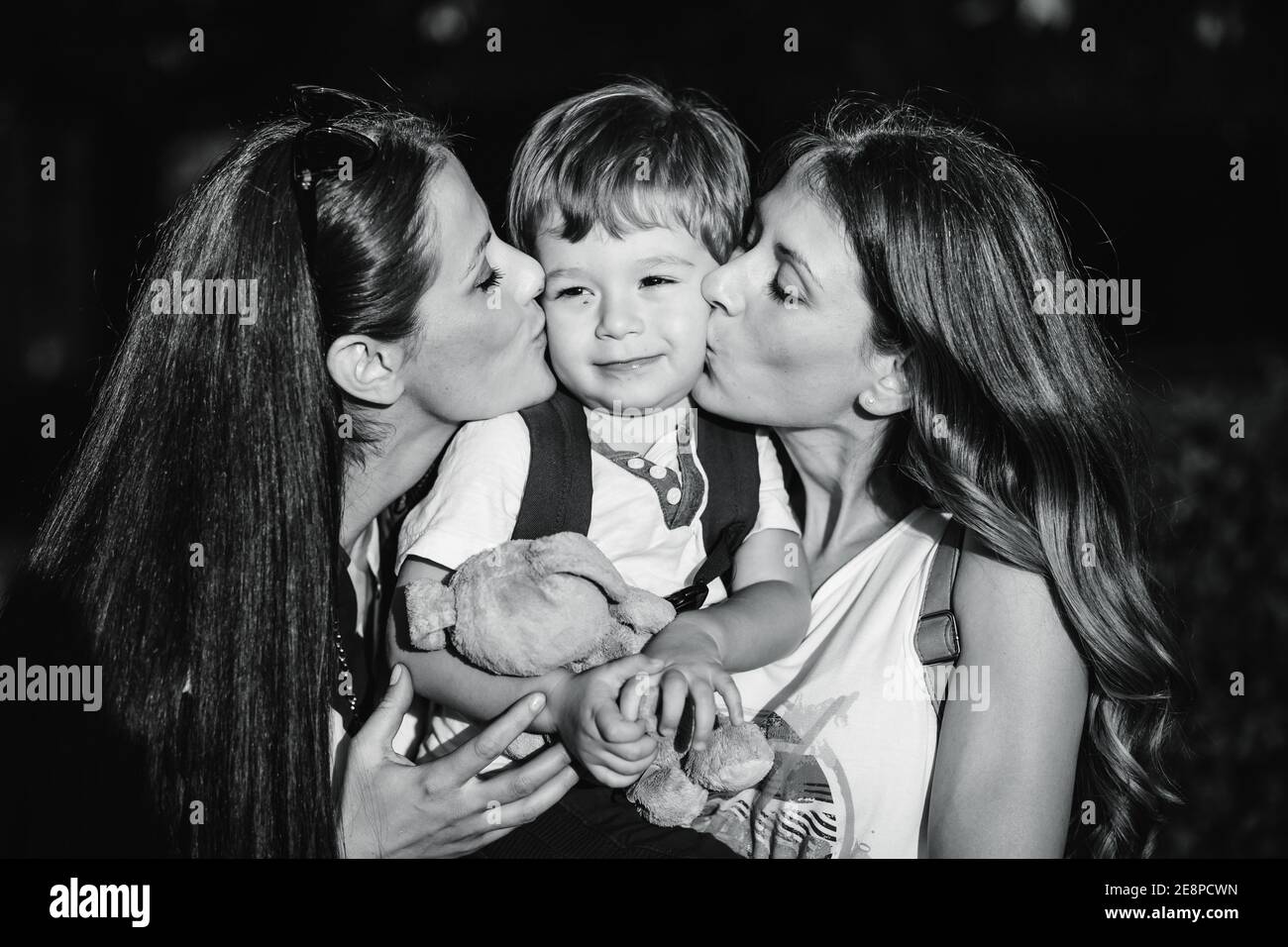 Black and white photo of mom and aunt holding and kissing a cute, little boy. Family love Stock Photo