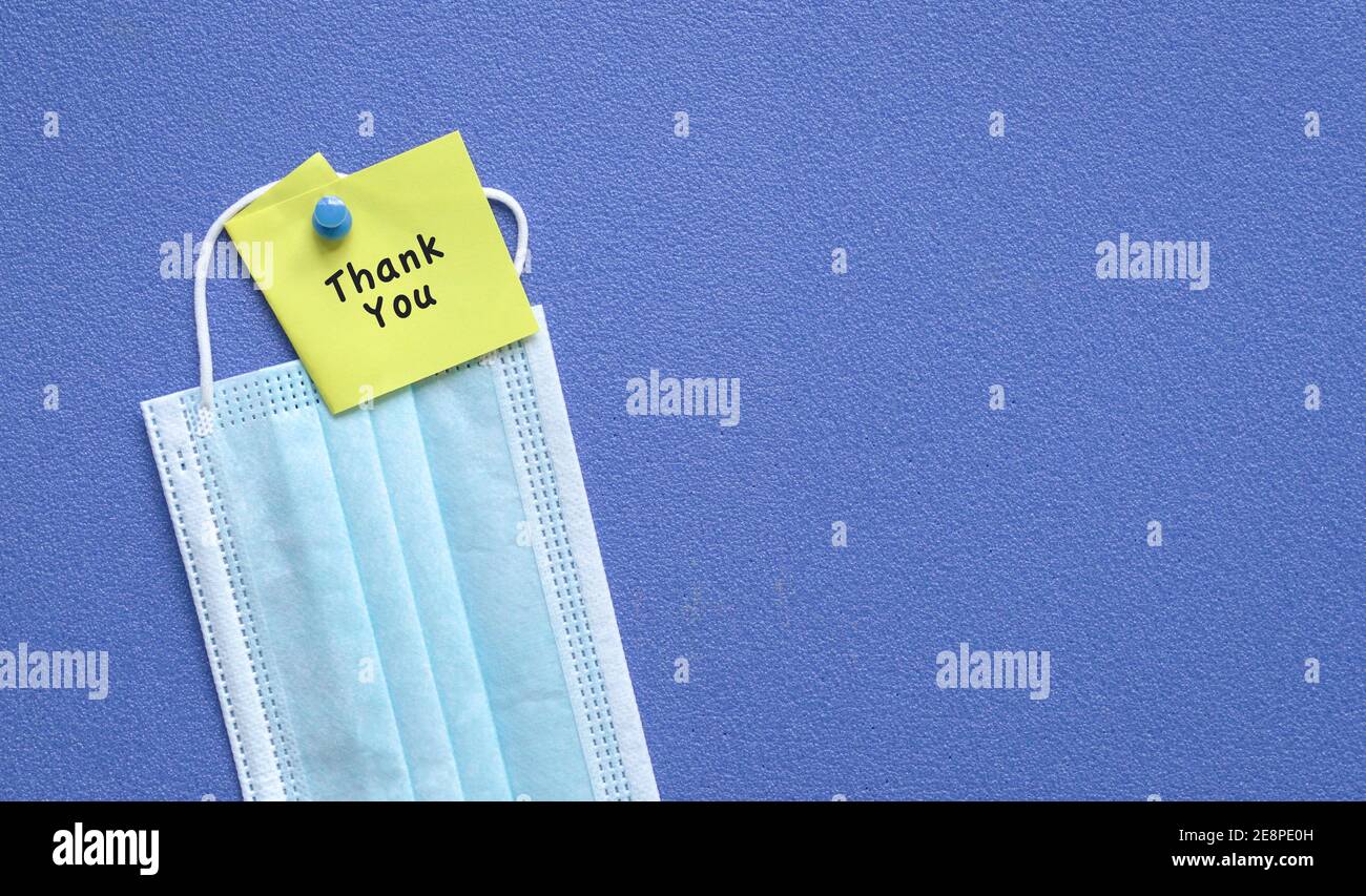 Thank you note on top of medical face mask. Pin on blue board. Copy space. Stock Photo