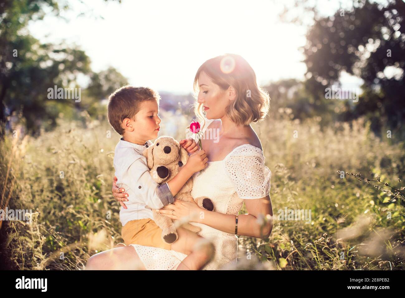 Beautiful young mom holding her blond son in her arms. Outdoor photo. Mothers day Stock Photo