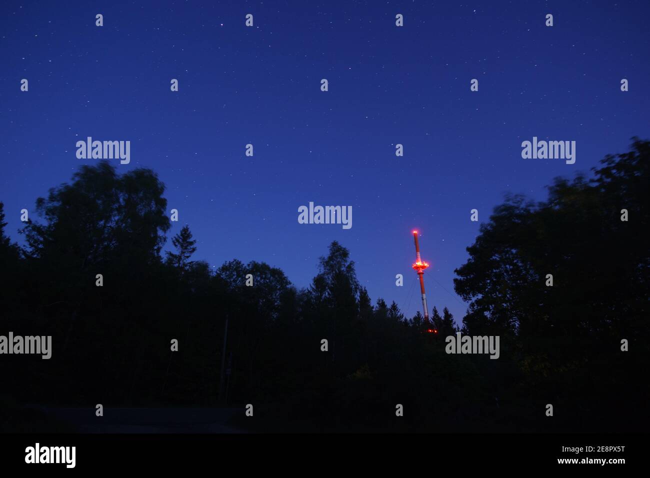 Radio tower at night with stars and silhouette of trees in the forest Stock Photo
