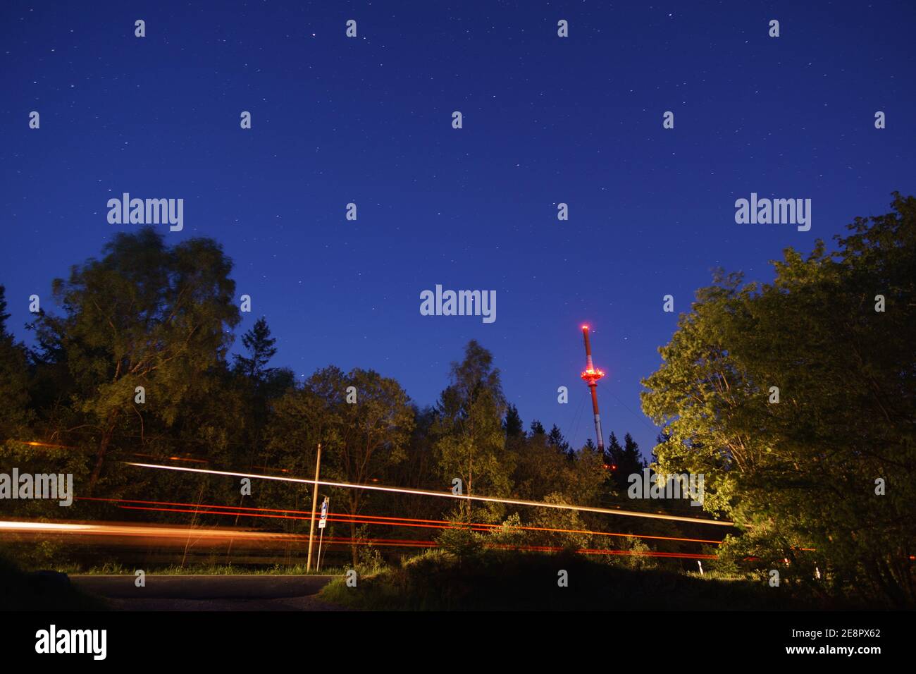 Radio tower at night and silhouette of trees in the forest with road and traffic made light trace Stock Photo
