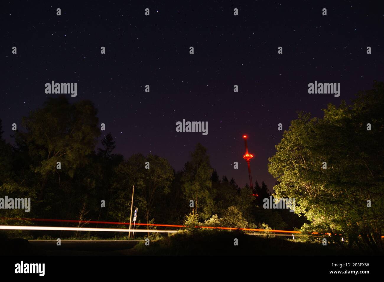 Radio tower at night and silhouette of trees in the forest with road and traffic made light trace Stock Photo