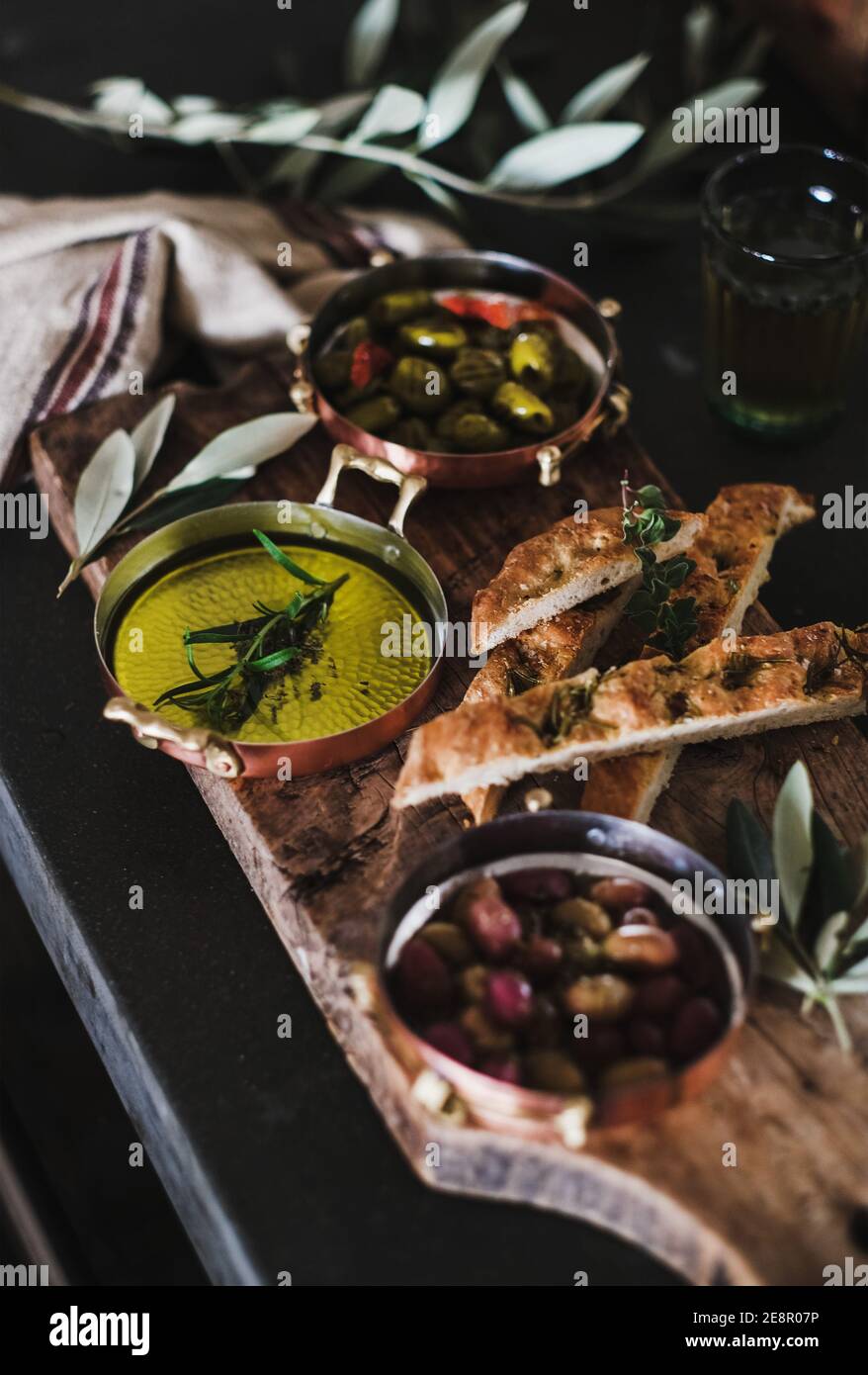 Pickled Greek olives, olive oil and herbed focaccia slices on rustic wooden board, selective focus. Traditional Mediterranean meze appetizers platter Stock Photo