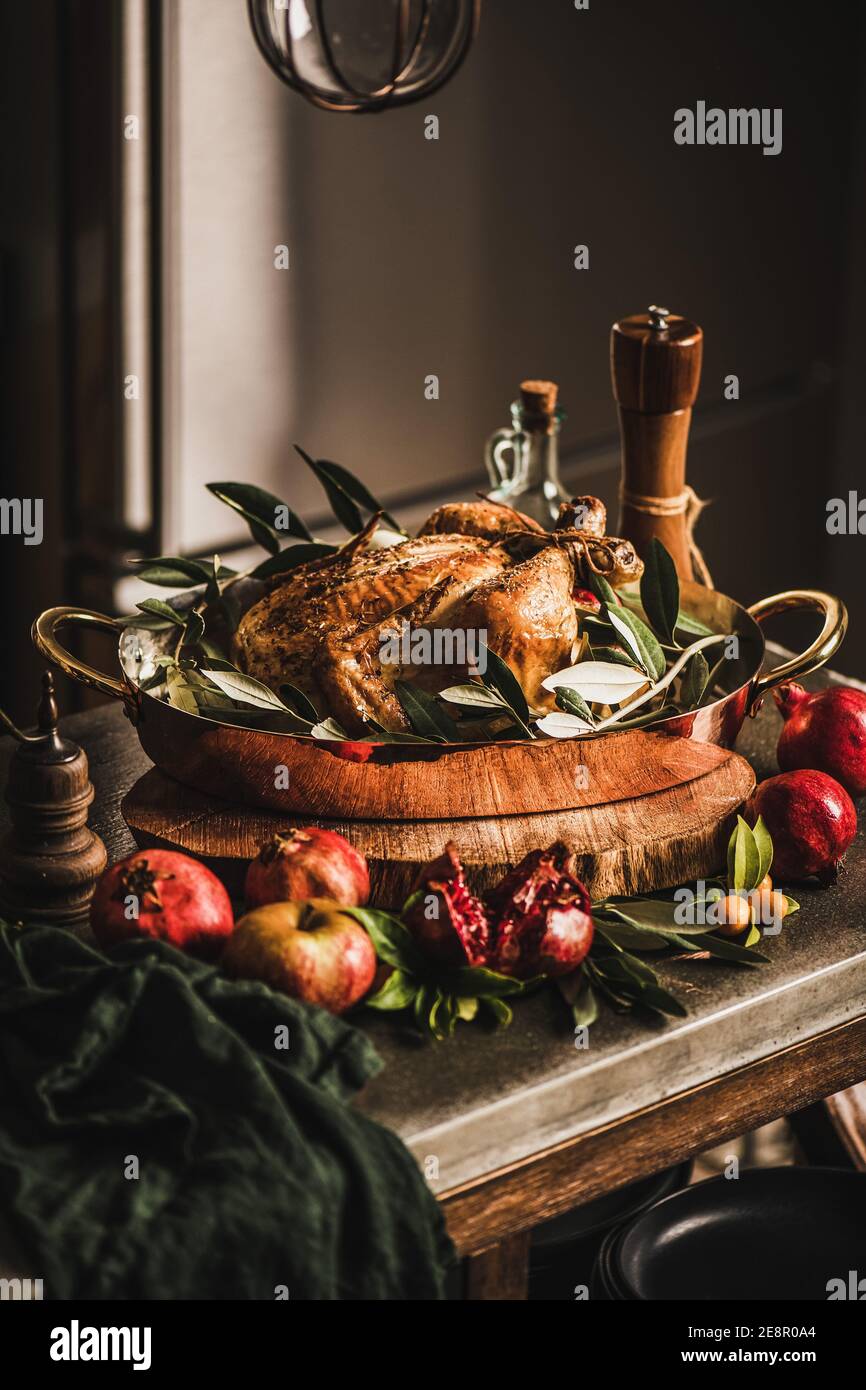 Whole roasted chicken for winter holiday festive dinner in copper roasting tin with spices, herbs and fruit on kitchen counter. Christmas or Thanksgiving Day cooking concept Stock Photo