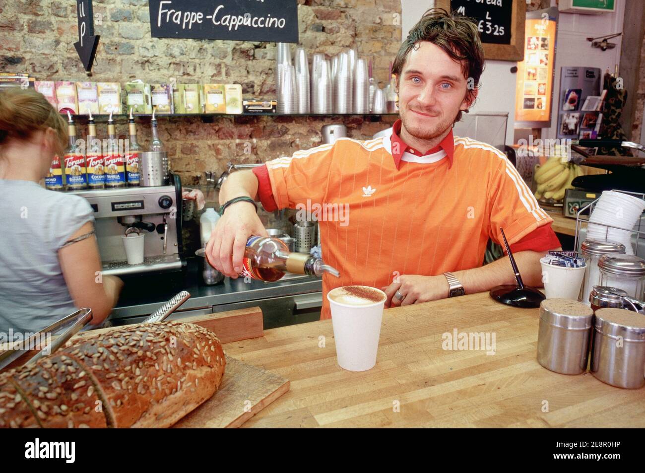 A male barista serving a cup of coffee spiked with a shot of amaretto liqueur at the counter of trendy cafe in East London Bricklane , Uk . Stock Photo