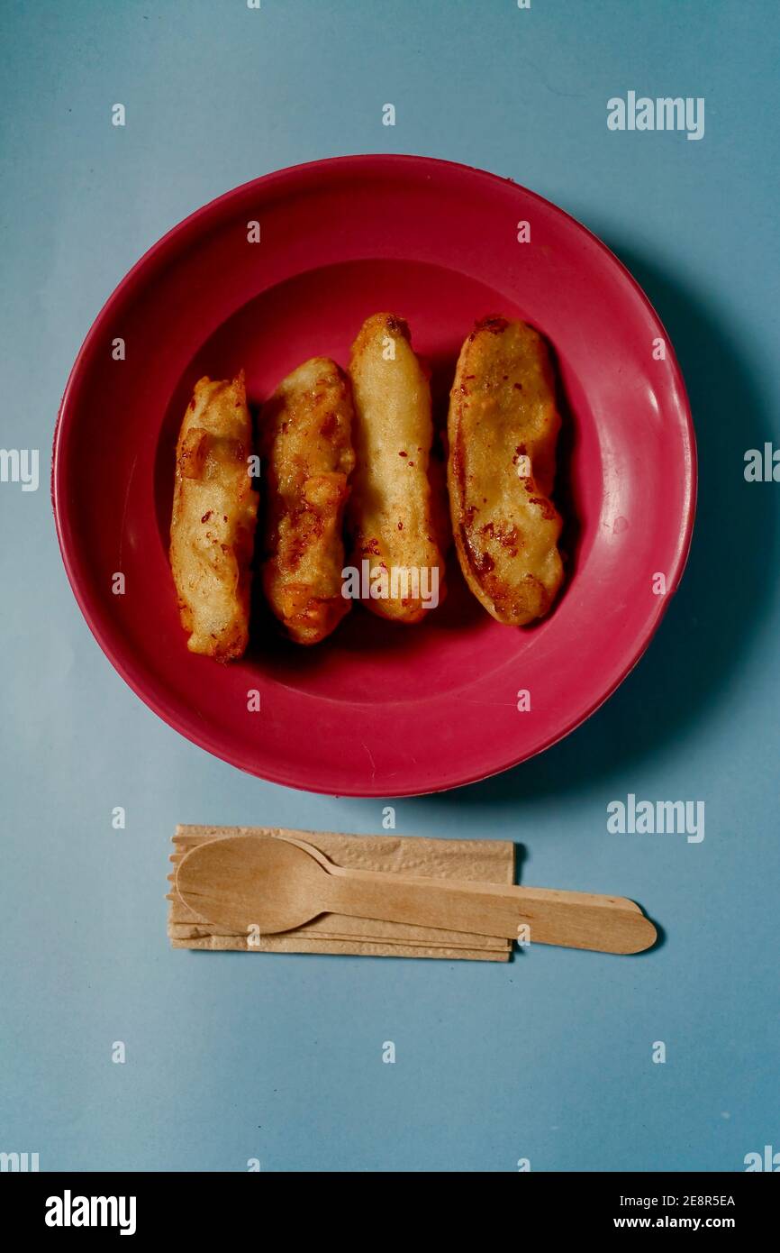 banana fried on red plate with wooden utensil isolated on blue background Stock Photo