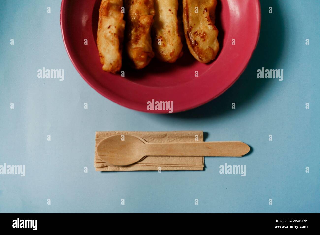 banana fried on red plate with wooden utensil isolated on blue background Stock Photo